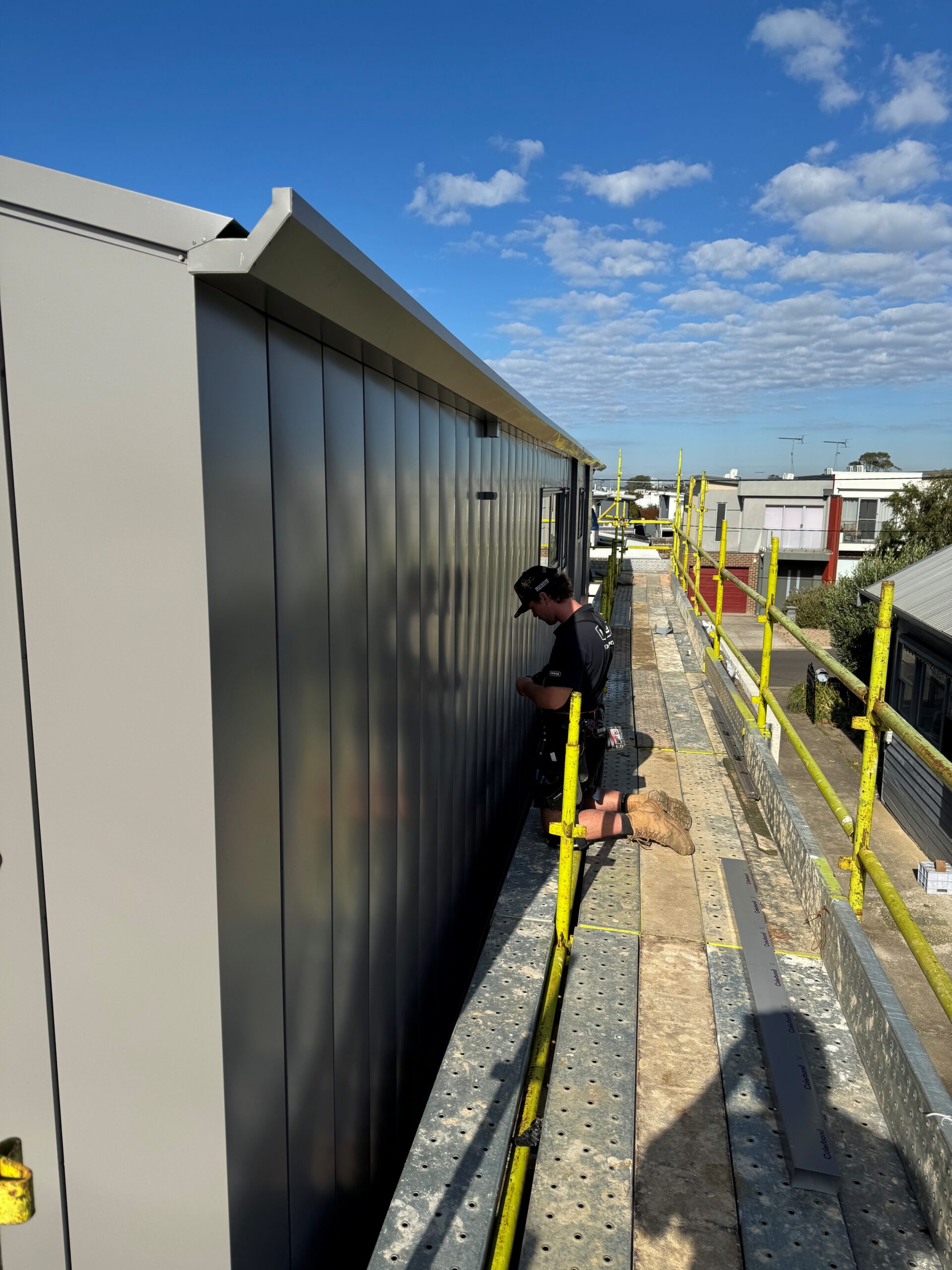 Installing custom interlocking architectural wall cladding in Colorbond Wallaby on a coastal home in Torquay Victoria